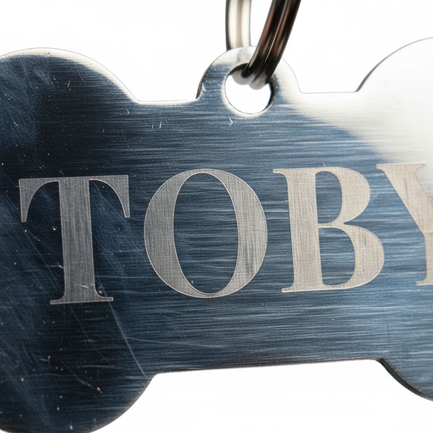 A close-up view of a metal dog tag with the name "TOBY" engraved on it.