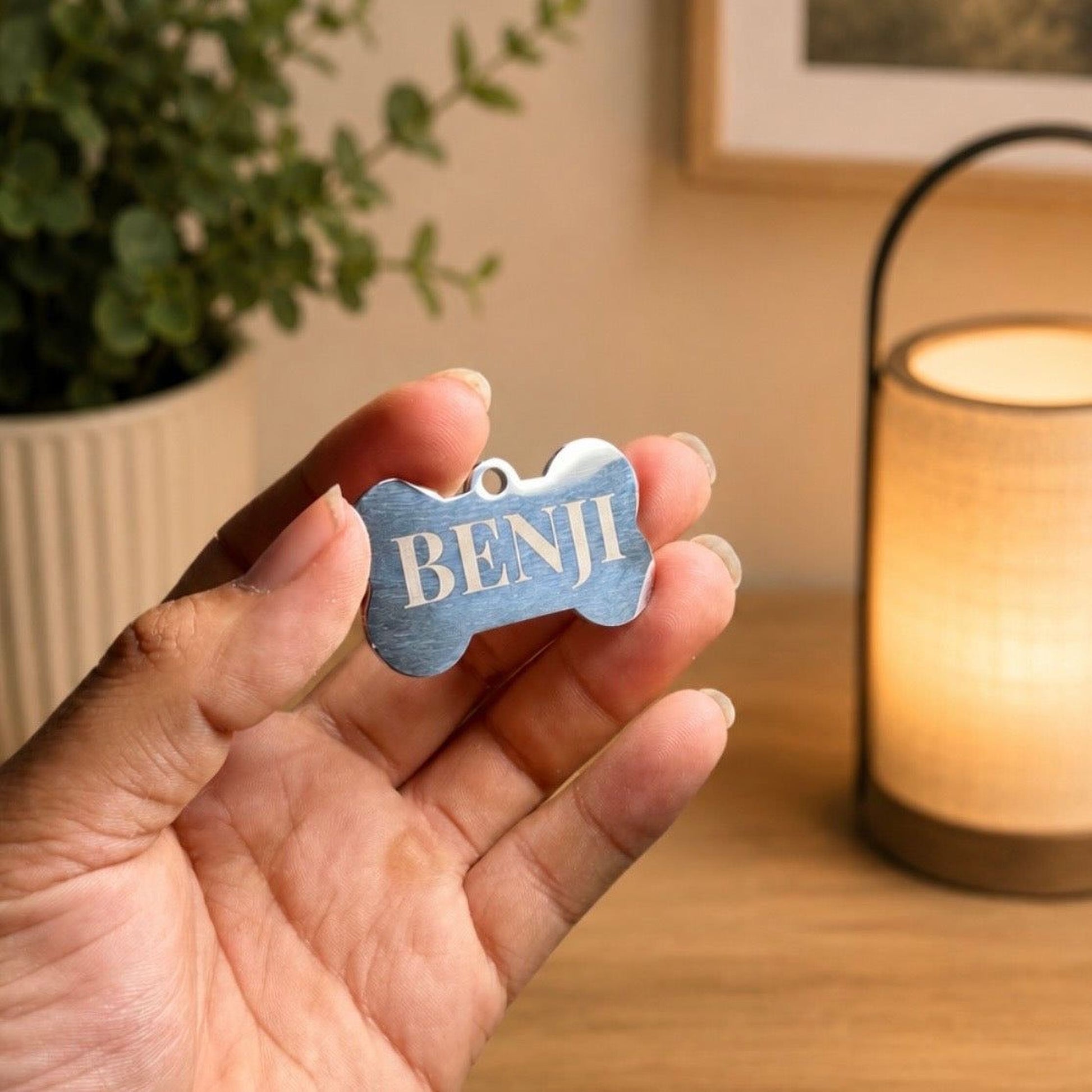 A hand holding a small metal dog tag with the name "BENJ" on it.