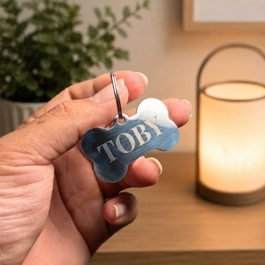 A person's hand holding a personalized dog tag with the name "TOBY" engraved on it.