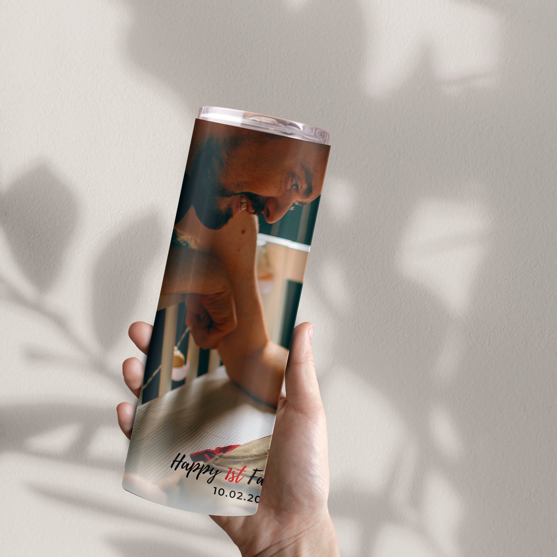 A person's hand holding a cylindrical object with a printed image of a man and a child on it, against a white wall background.