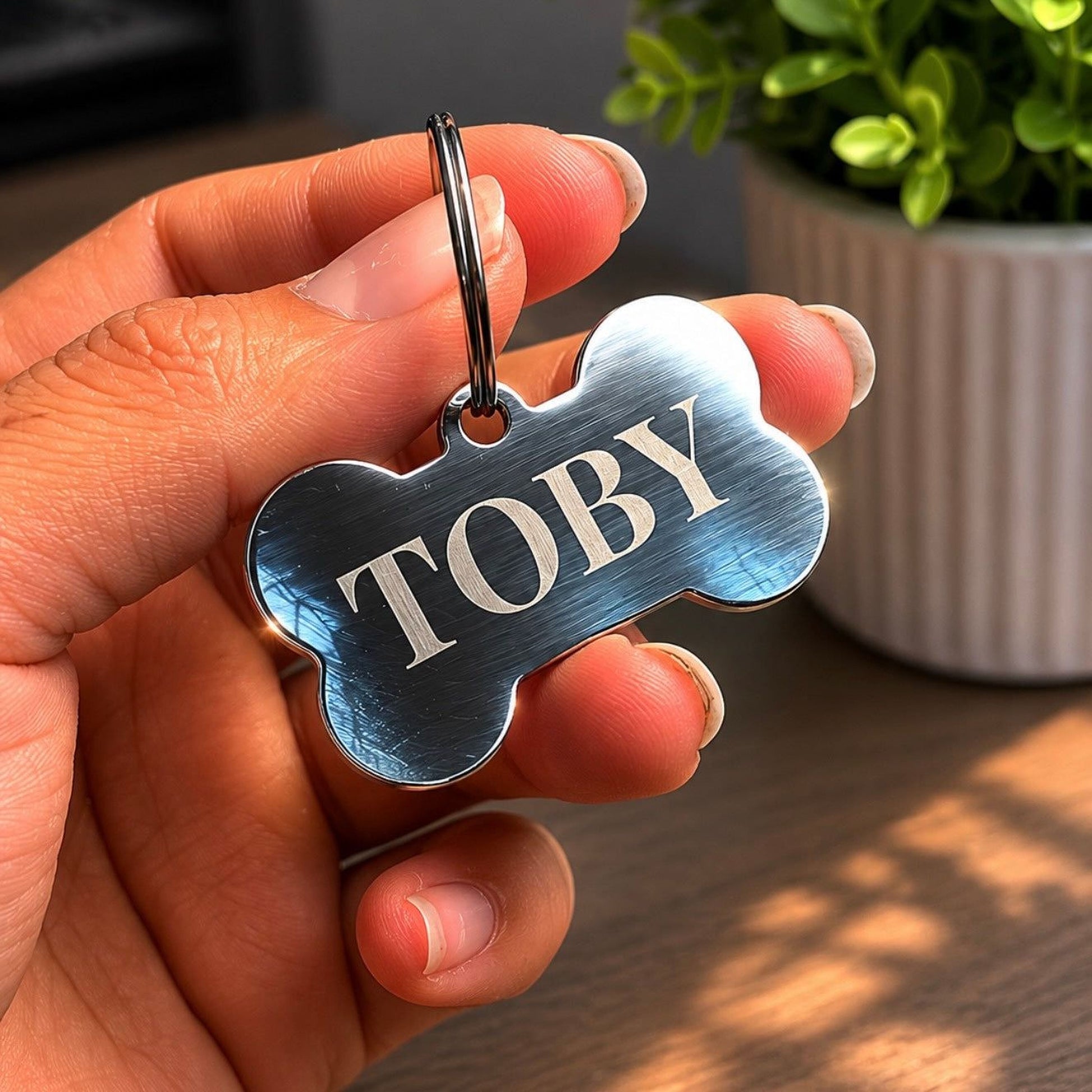 A person's hand holding a personalized dog tag with the name "Toby" engraved on it.