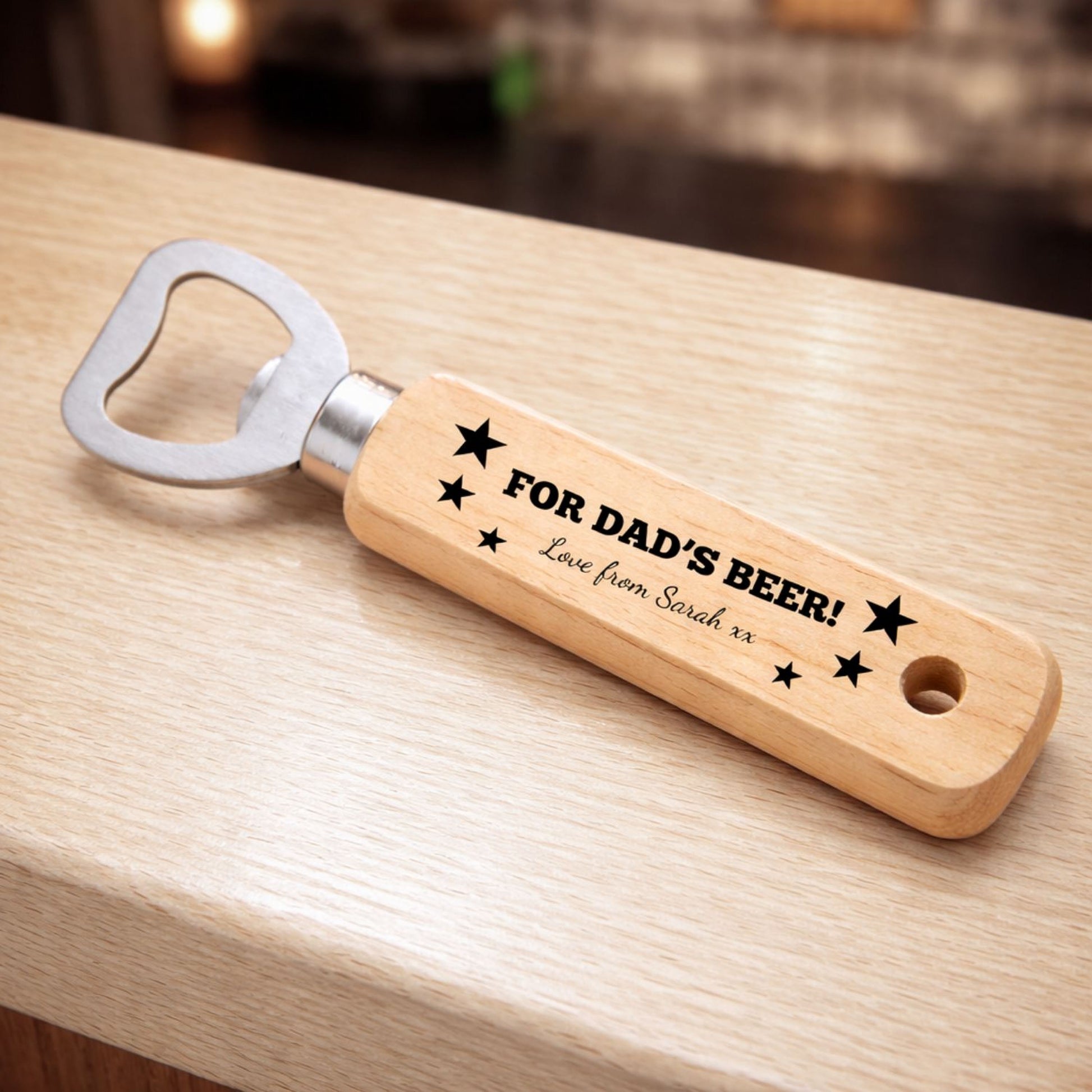 A wooden bottle opener with a personalized message engraved on it, resting on a wooden surface.