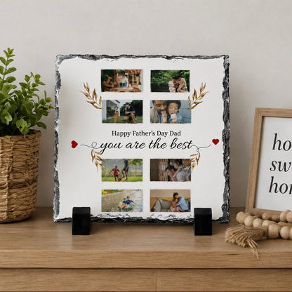 A square photo frame displaying a collage of family photos with the text "Happy Father's Day Dad, you are the best" written on it. The frame is placed on a wooden shelf, with a potted plant and a wooden bead display nearby.