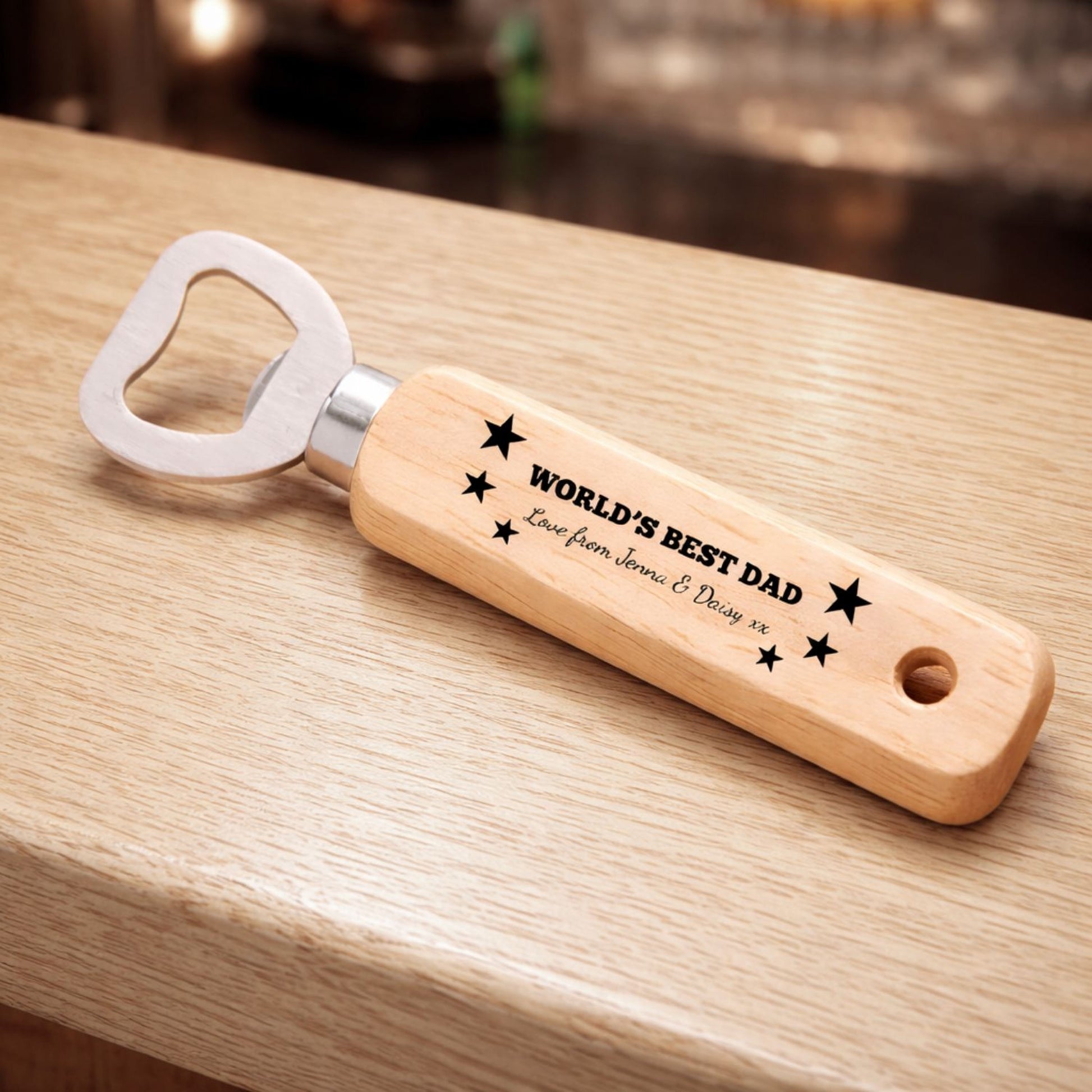 A wooden bottle opener with a personalized message engraved on it, sitting on a wooden surface.