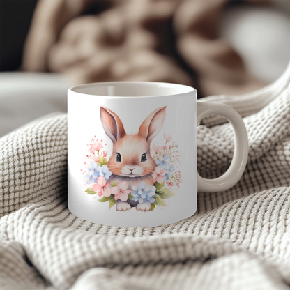 A white ceramic mug with a floral design featuring a cute bunny rabbit surrounded by colorful flowers.