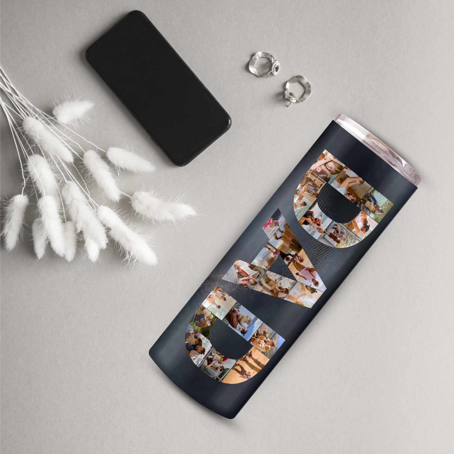 a black tumbler with the word "DAD" written on it, along with a smartphone and earrings.