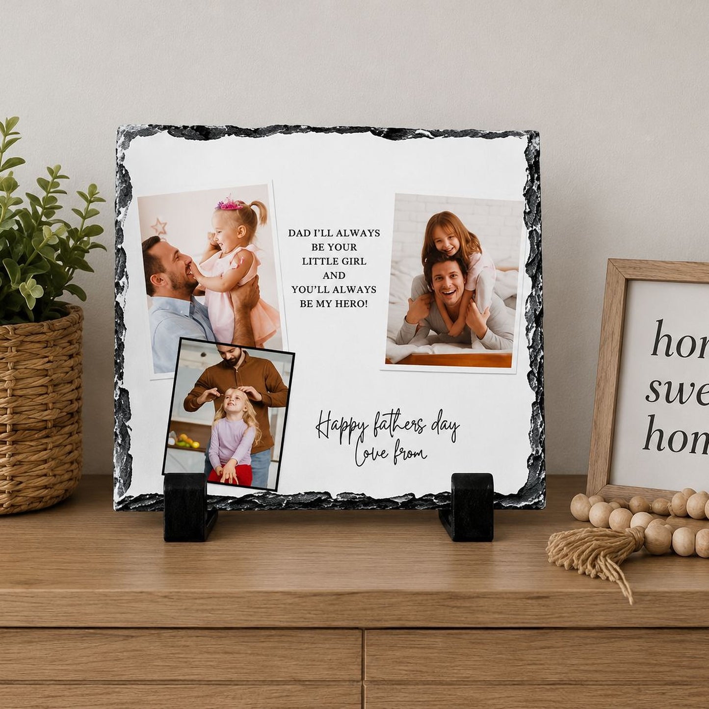 A black and white photo frame displaying a collage of three photographs, along with a message that reads "Happy fathers day love from". The frame is placed on a wooden surface, with a potted plant and a beaded decoration to the side.