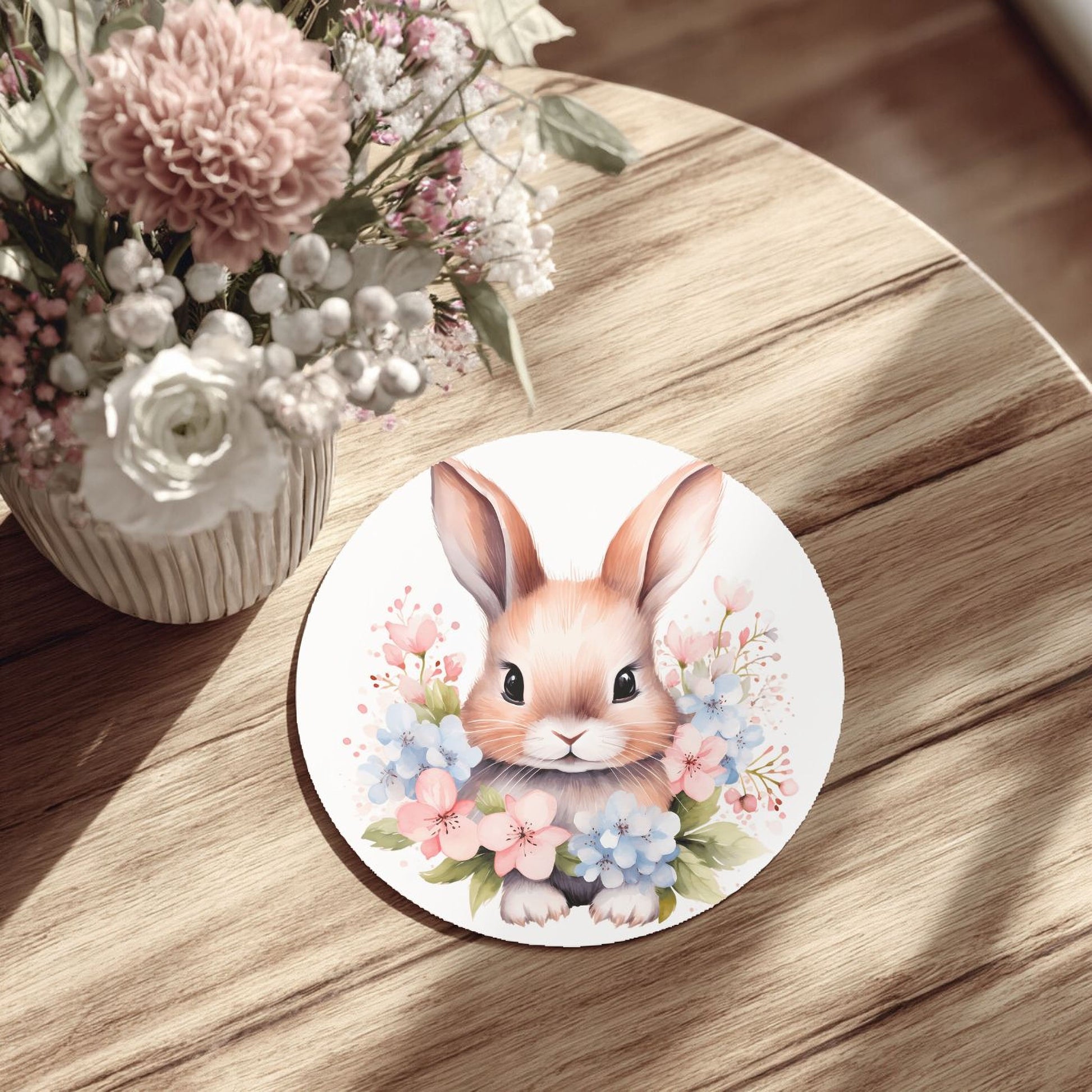 a round white plate with a picture of a bunny surrounded by flowers, placed on a wooden table.