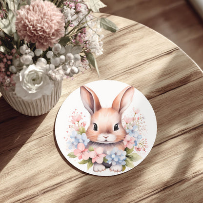 a round white plate with a picture of a bunny surrounded by flowers, placed on a wooden table.