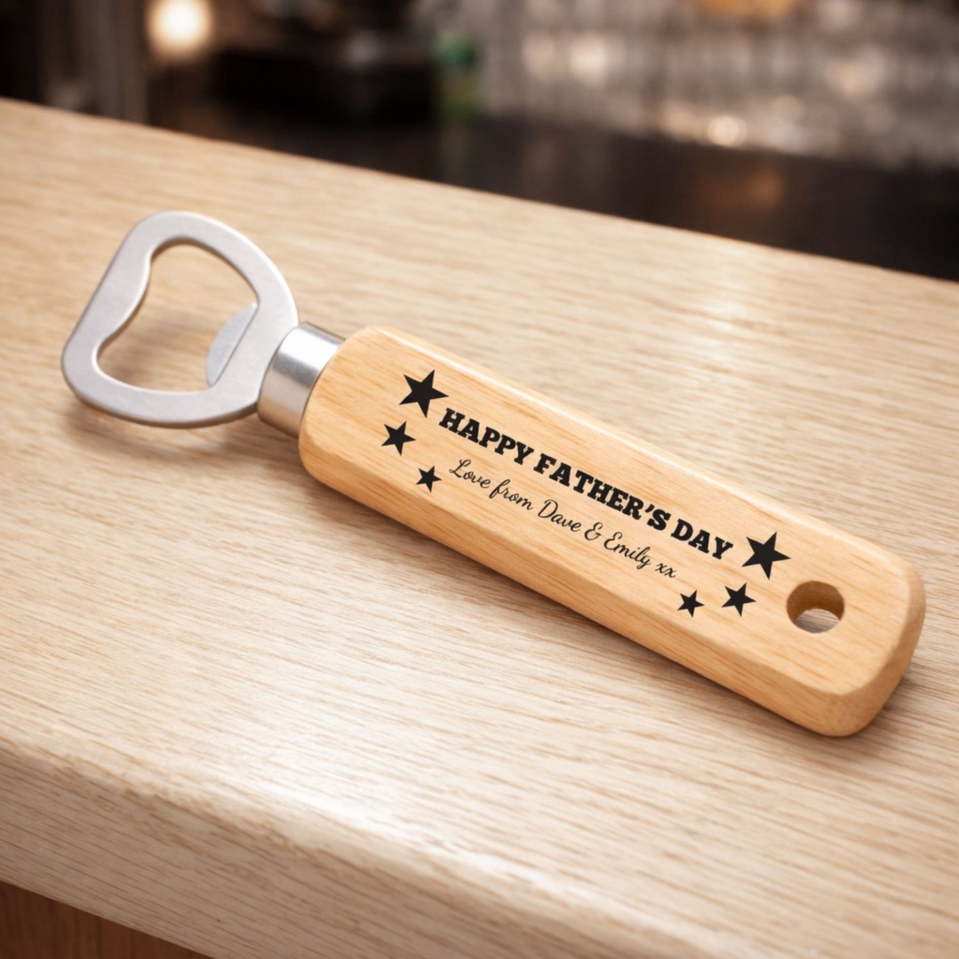 A wooden bottle opener with a personalized message engraved on it, sitting on a wooden surface.