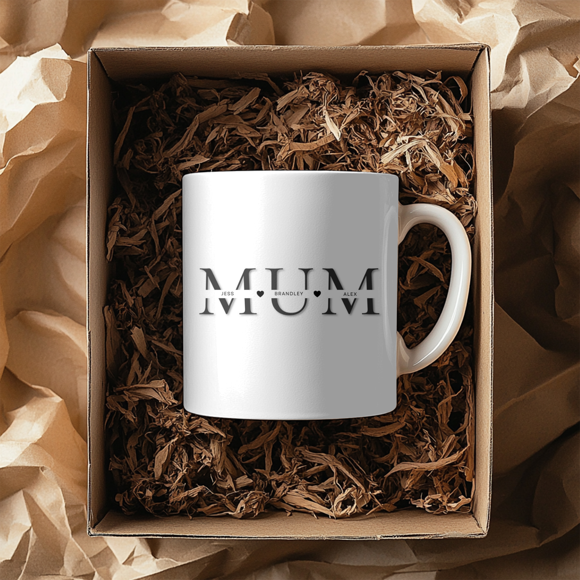 A white mug with the word "MUM" printed on it, placed inside a cardboard box filled with shredded paper.